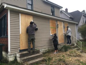 Volunteers Aimee Robertson-Fant, Kyle Johson, and Augusta Wray work to cover plywood securing the abandoned home at 710 N. Mulberry St.