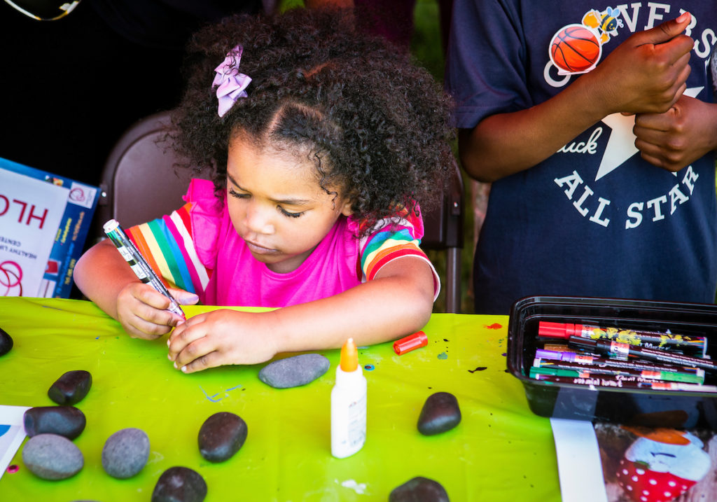 Little girl sits at a table. It is covered with rocks and crafting supplies