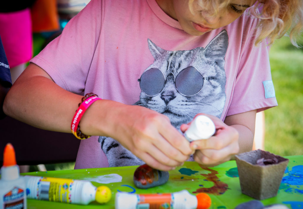 A young girl decorates a rock with rainbow colors