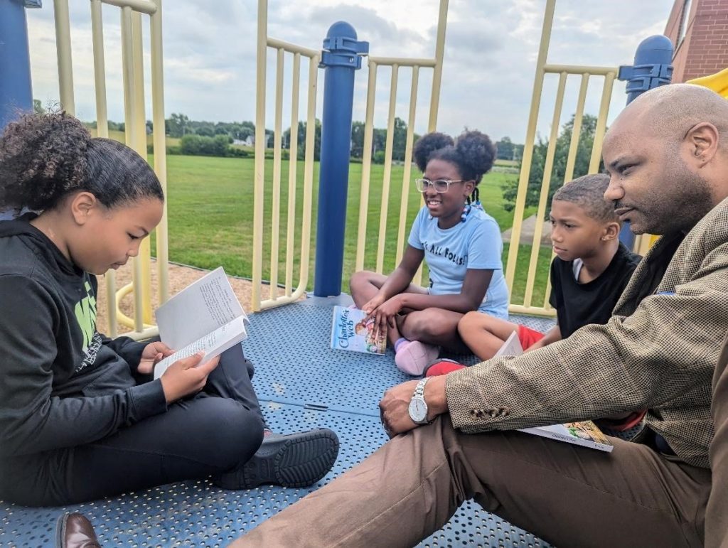Longfellow Elementary School student Isabella Foster reads Charlotte’s Web to Longfellow Principal Gerry Moore and her schoolmates A’Nyiah Shannon and Rashaud Hill. 